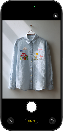 An iPhone camera taking a basic photo of a light blue embroidered shirt on a hanger — the only photo PhotoLotus needs to start